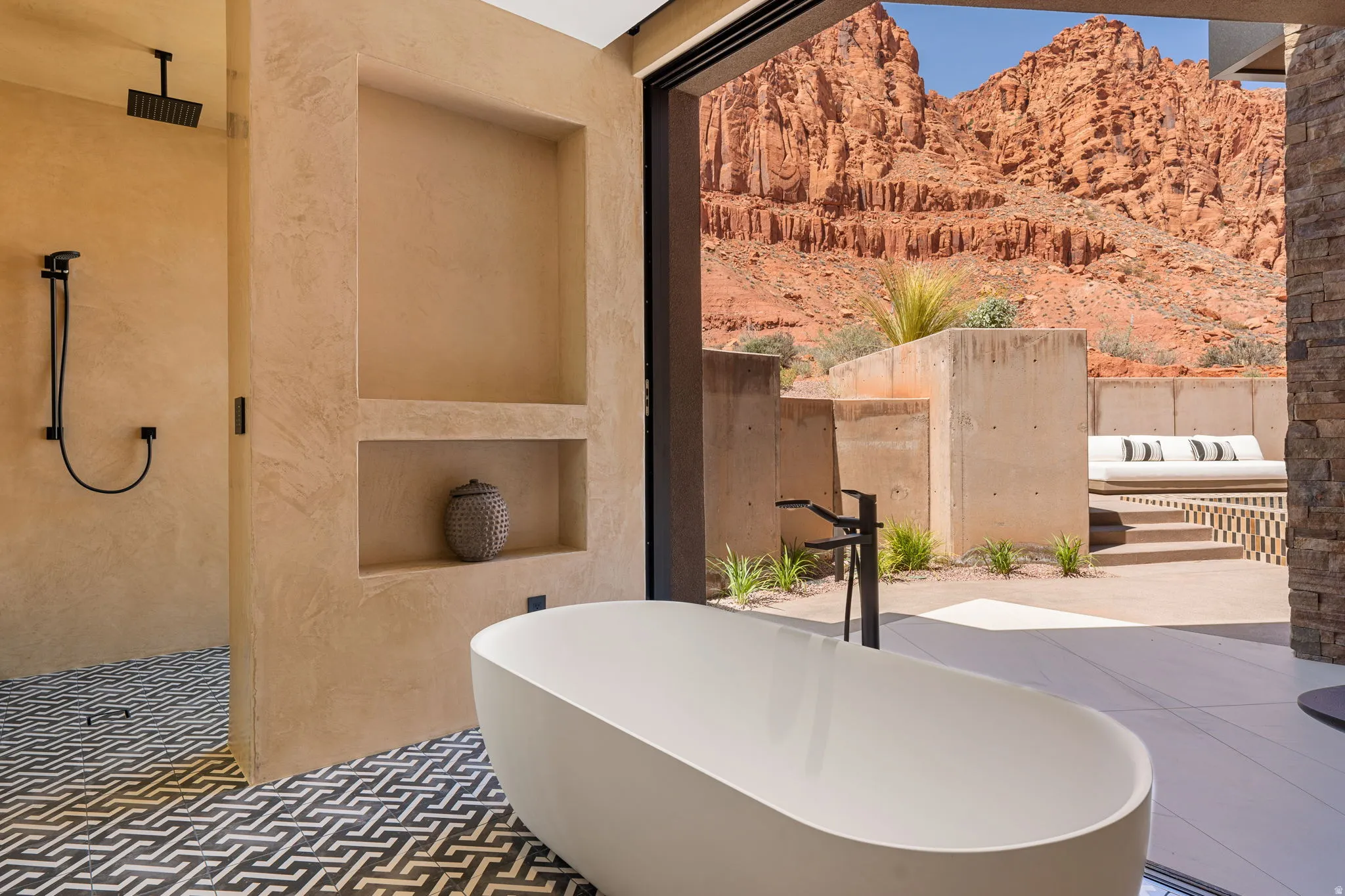 Freestanding soaking tub with matte black floor-mounted faucet, geometric tile flooring, walk-in shower with rain showerhead, and built-in wall niches