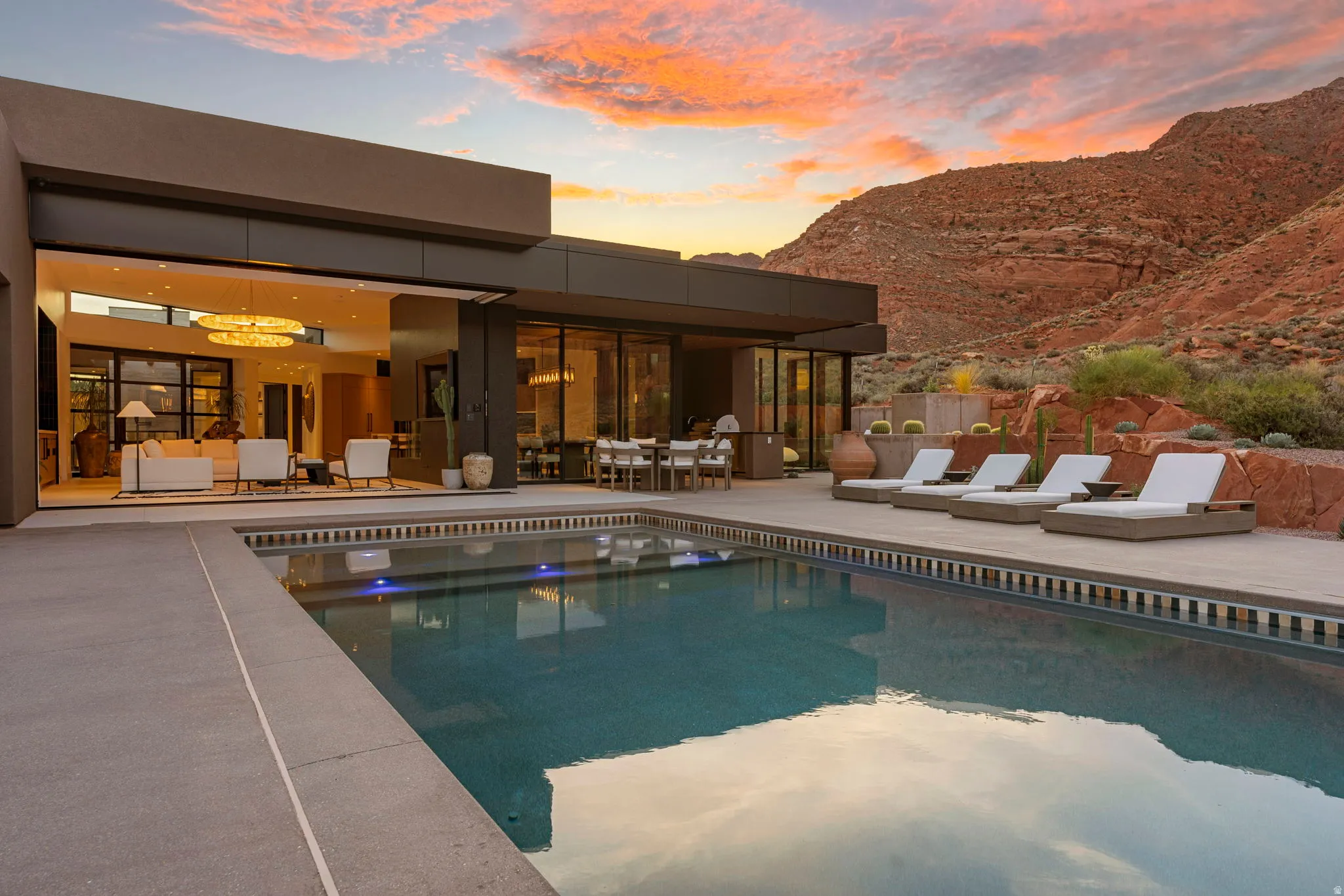 Modern architecture with expansive glass sliders, outdoor swimming pool, integrated patio dining area, and mountain backdrop
