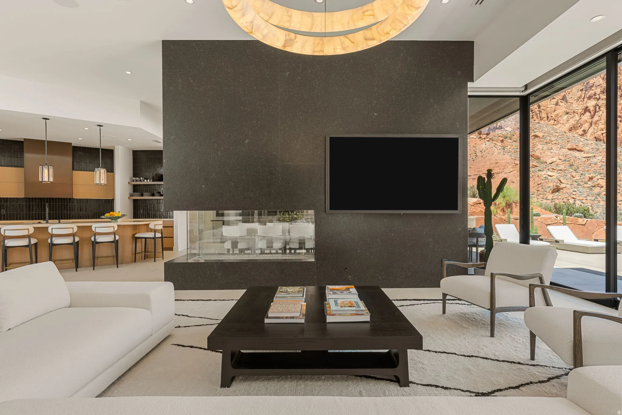 Spacious interior featuring a stone-clad fireplace and media wall, large format glass windows, and a built-in kitchen island with pendant lighting