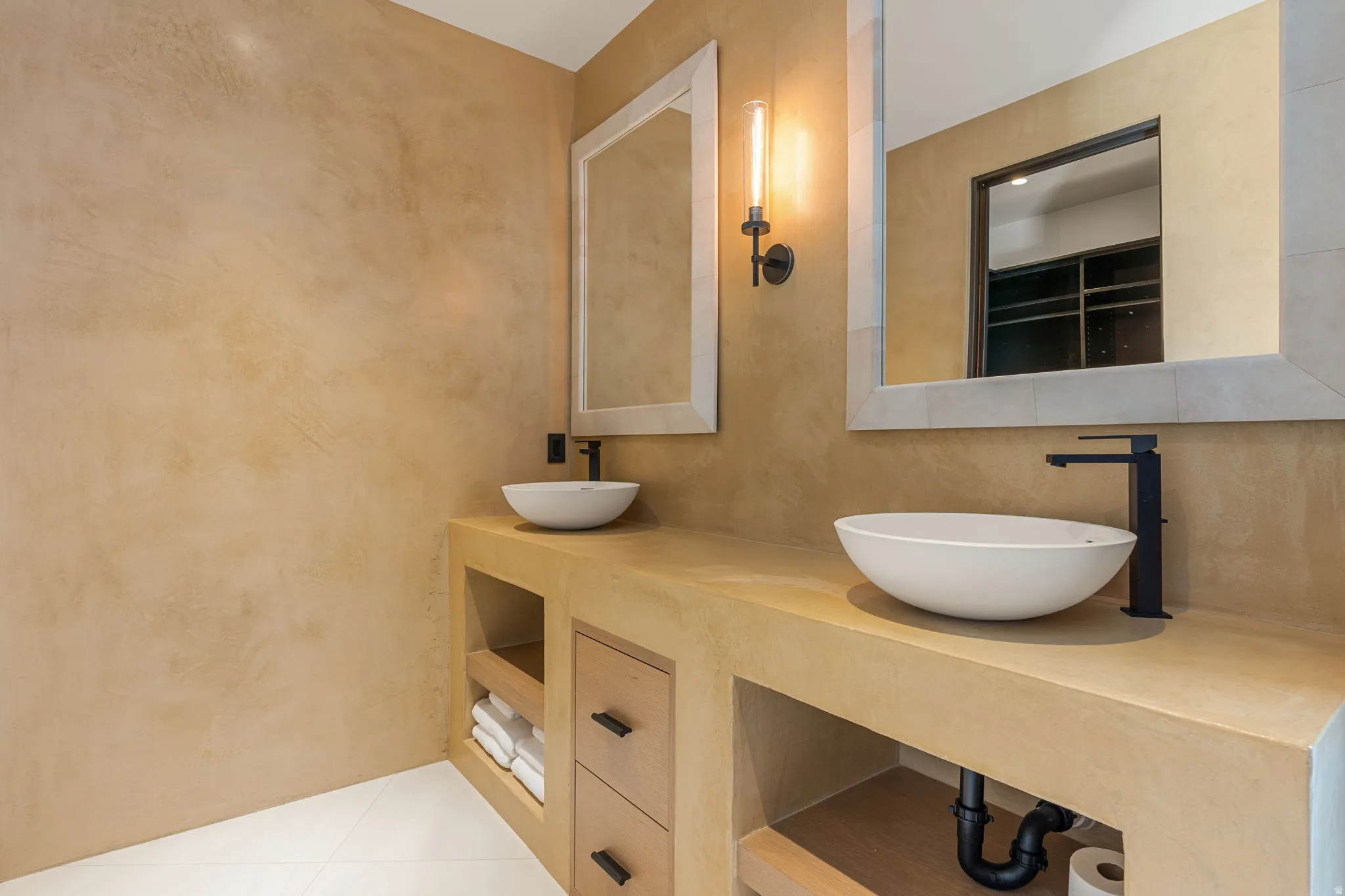 Dual vessel sinks with matte black fixtures, integrated countertop, wood-finish cabinetry, and textured wall finish