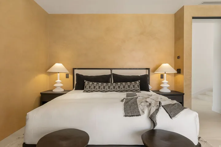 Textured wall finish, built-in recessed lighting, dark wood-finish nightstands, upholstered bed frame, and light flooring