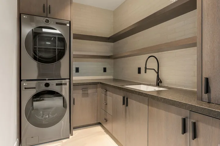 Built-in cabinetry with dark hardware, undermount sink with a matte black faucet, and stacked washer and dryer