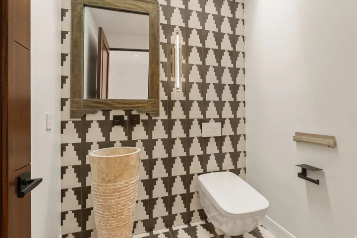 Powder room featuring a pedestal basin, wall-mounted toilet, decorative tile accent wall, and a framed mirror
