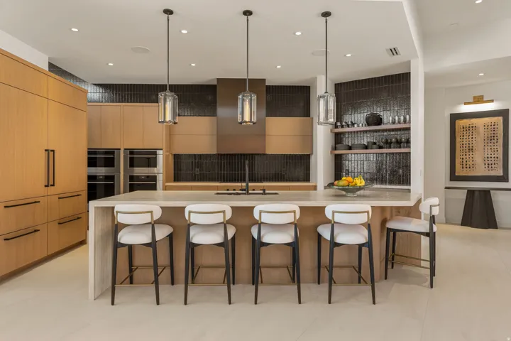 Central kitchen island with a light-toned countertop, integrated dual ovens, a dark tile backsplash, wood-finish cabinetry, and recessed lighting