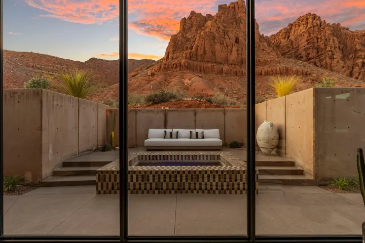Expansive glass doors opening to an outdoor patio with a tiled water feature, concrete retaining walls, and tiered hardscaping, all set against a backdrop of rugged red rock mountains
