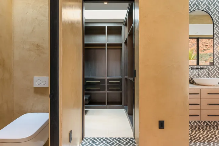 Built-in closet system, dual flush toilet, vanity with vessel sink, patterned floor tile, and wall-mounted faucet