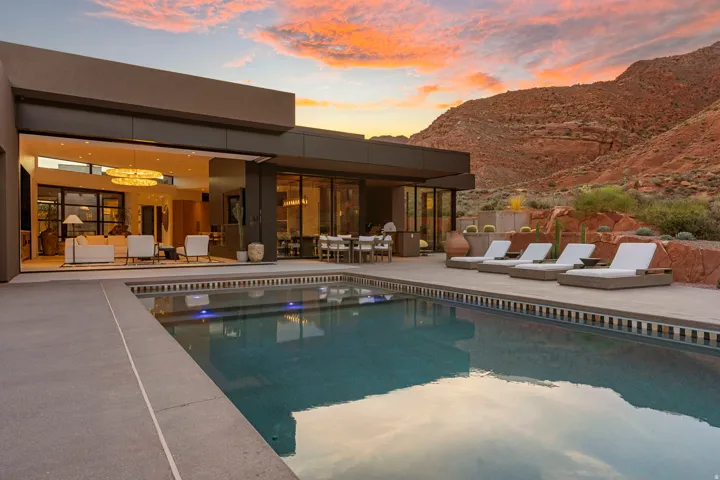 Modern architecture with expansive glass sliders, outdoor swimming pool, integrated patio dining area, and mountain backdrop