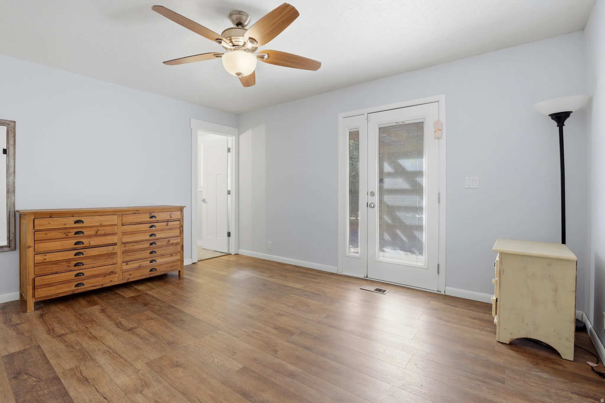 Wood-finish flooring with light gray walls, an overhead ceiling fan, and double doors featuring privacy glass