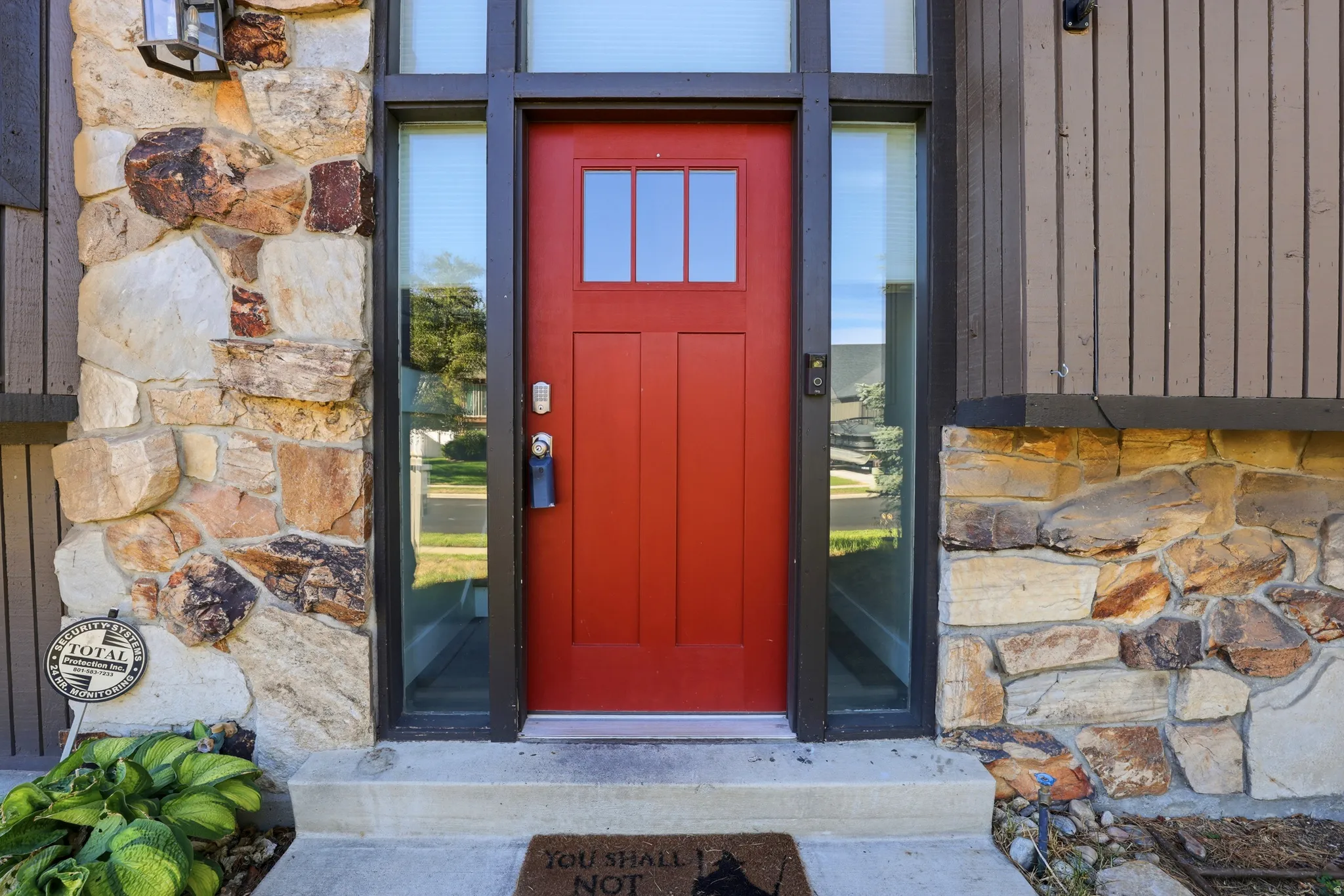 Red entry door with glass paneling, flanked by glass sidelights and stacked stone facade