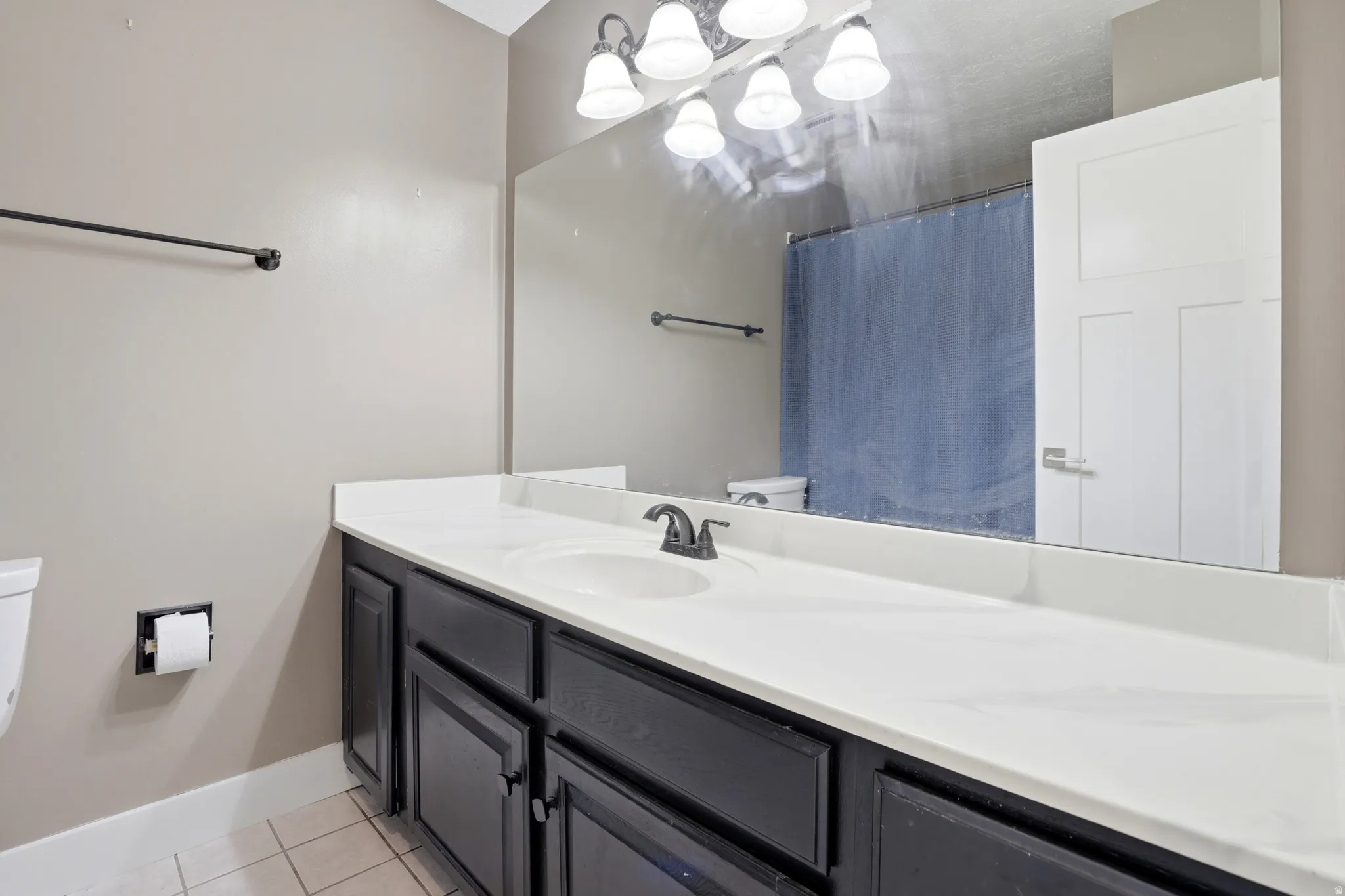 Vanity with integrated sink, expansive countertop, dark wood-finish cabinetry, and overhead sconce lighting