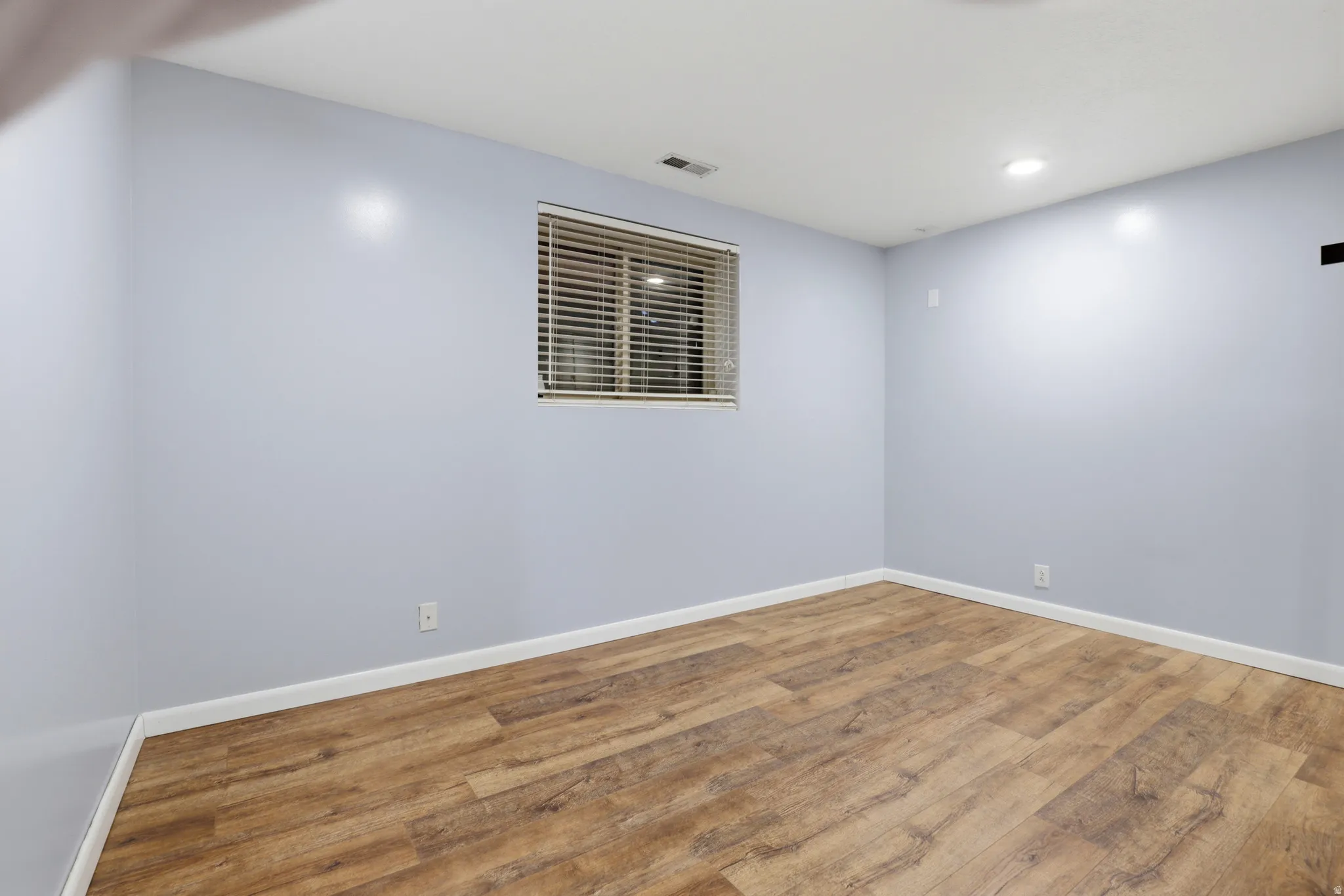 Recessed lighting illuminates wood-finish flooring and a window with horizontal blinds