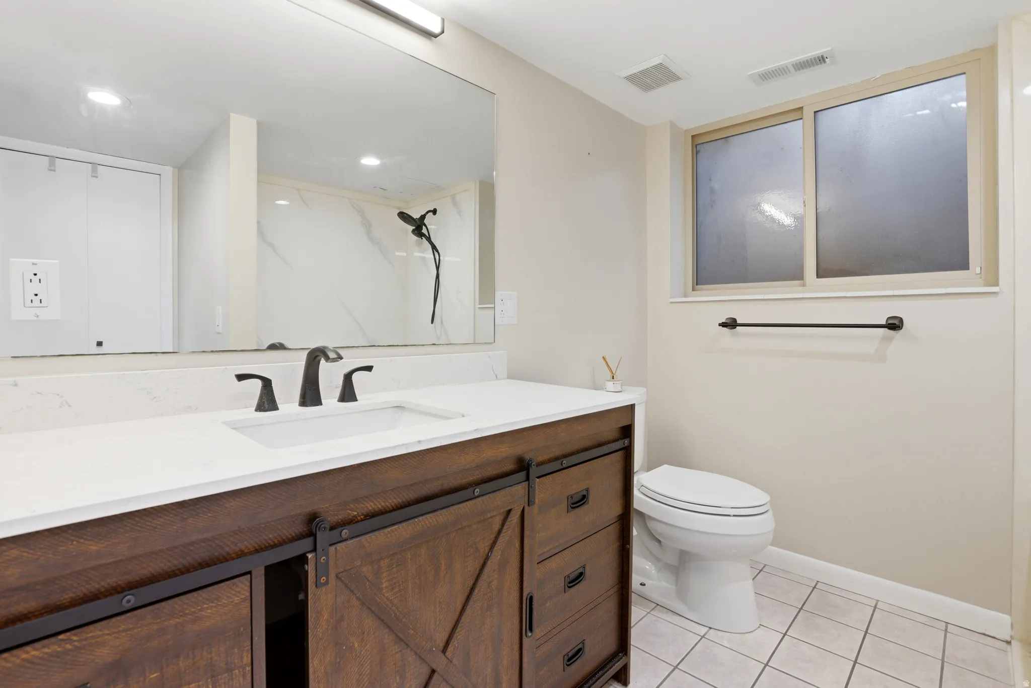Modern vanity with a white countertop and integrated sink, barn door style cabinet fronts, matte black fixtures, and a large mirror