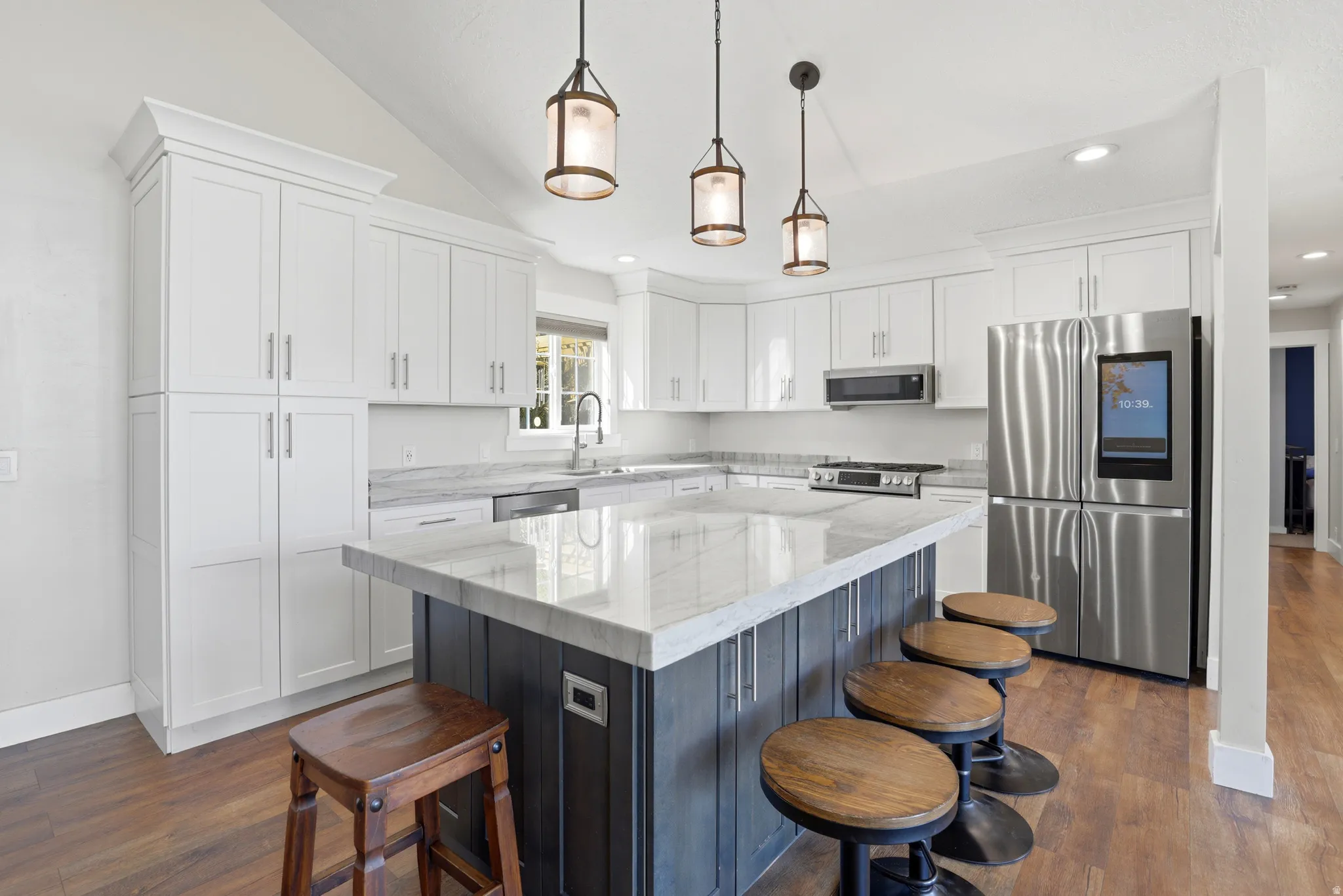 White cabinetry, large center island with seating, stainless steel appliances, wood-finish flooring, and vaulted ceiling