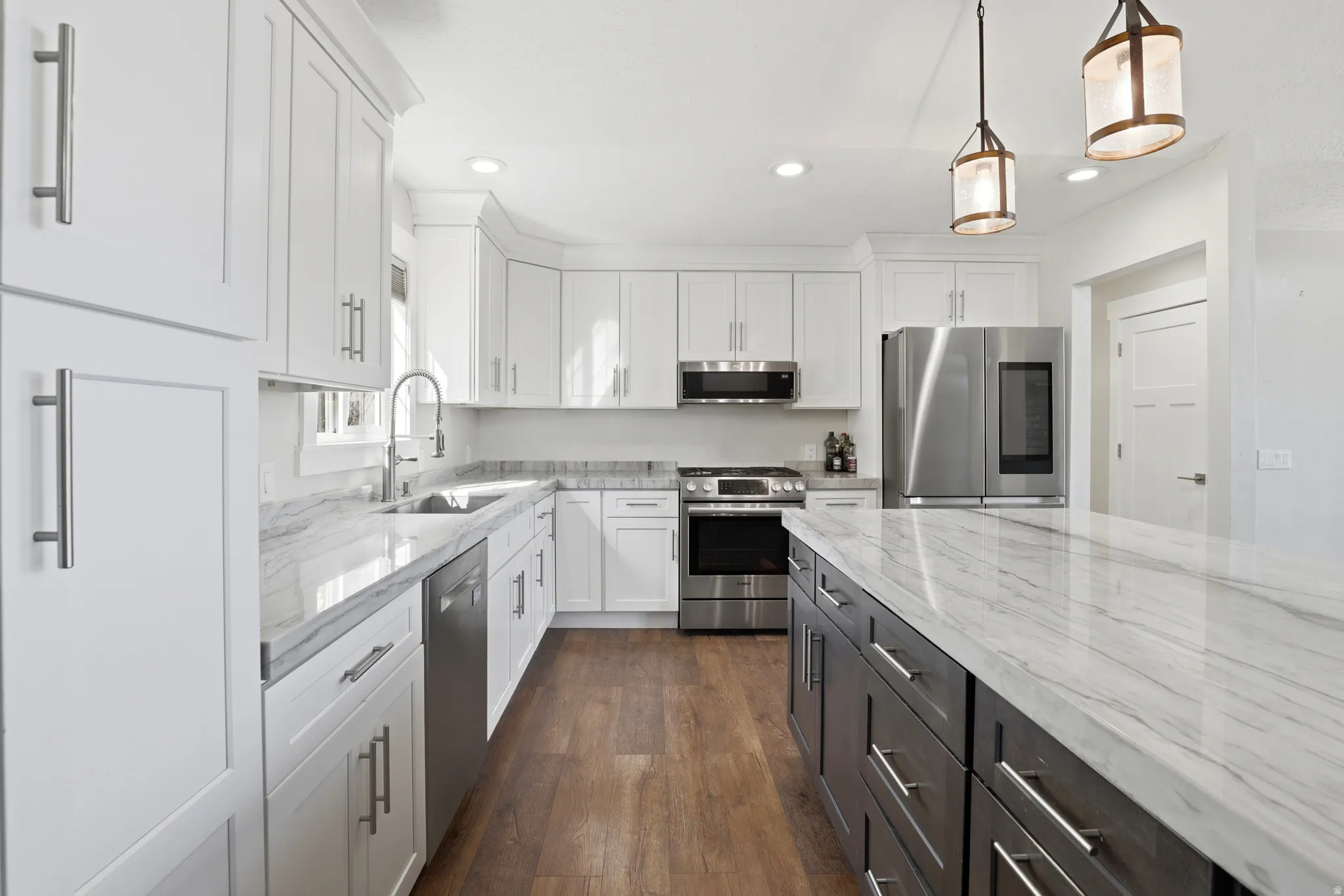 Kitchen featuring white shaker-style cabinetry, stainless steel appliances, wood-finish flooring, and light-toned countertops