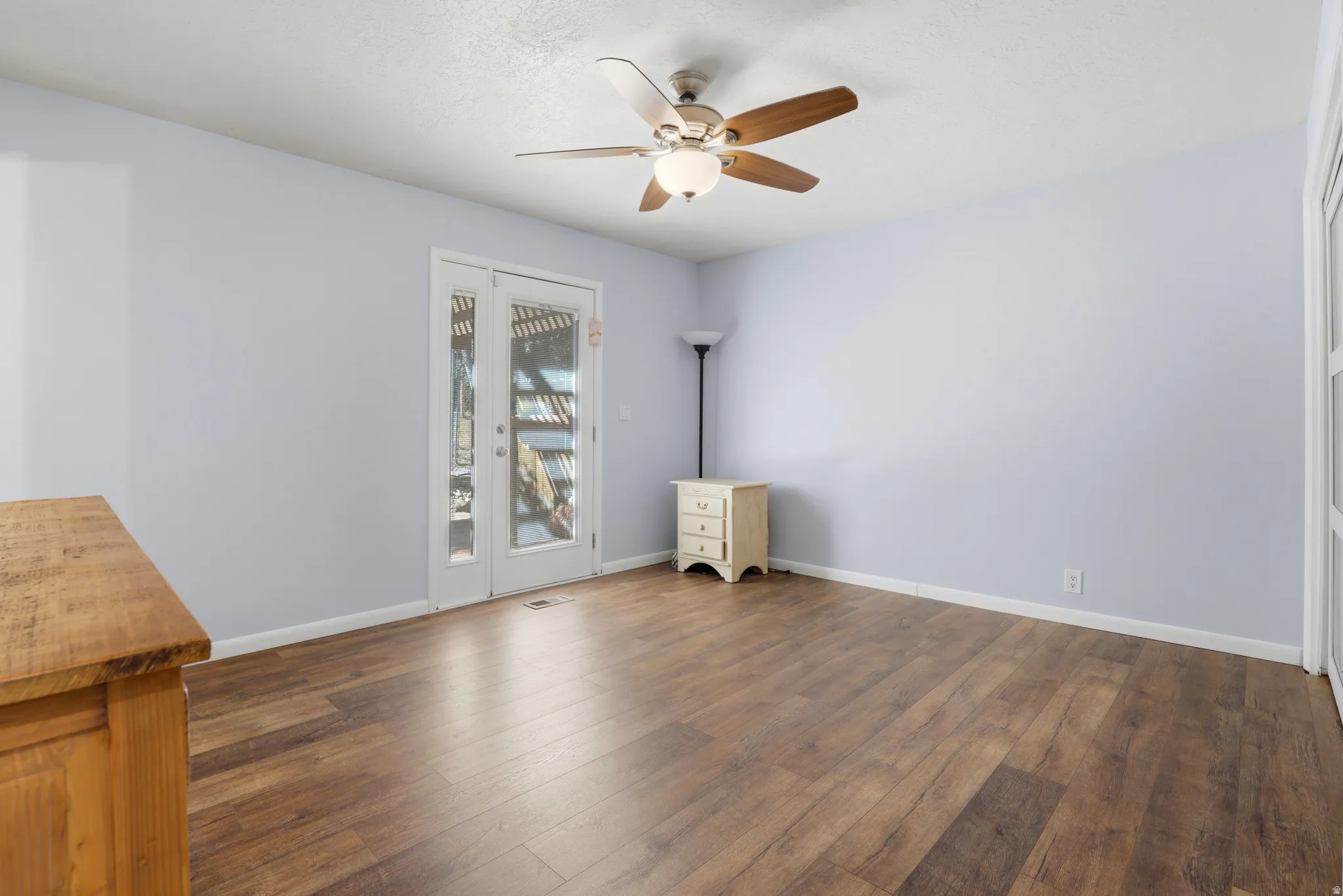 Wood-finish flooring, ceiling fan with integrated lighting, and a white double door with glass panels