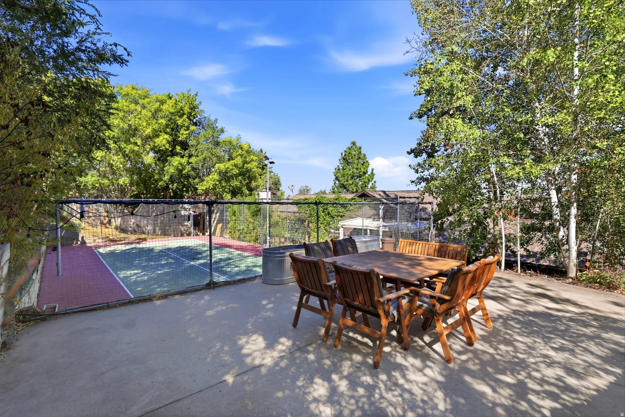 Paved patio area, dedicated sports court with net, established trees, and perimeter fencing