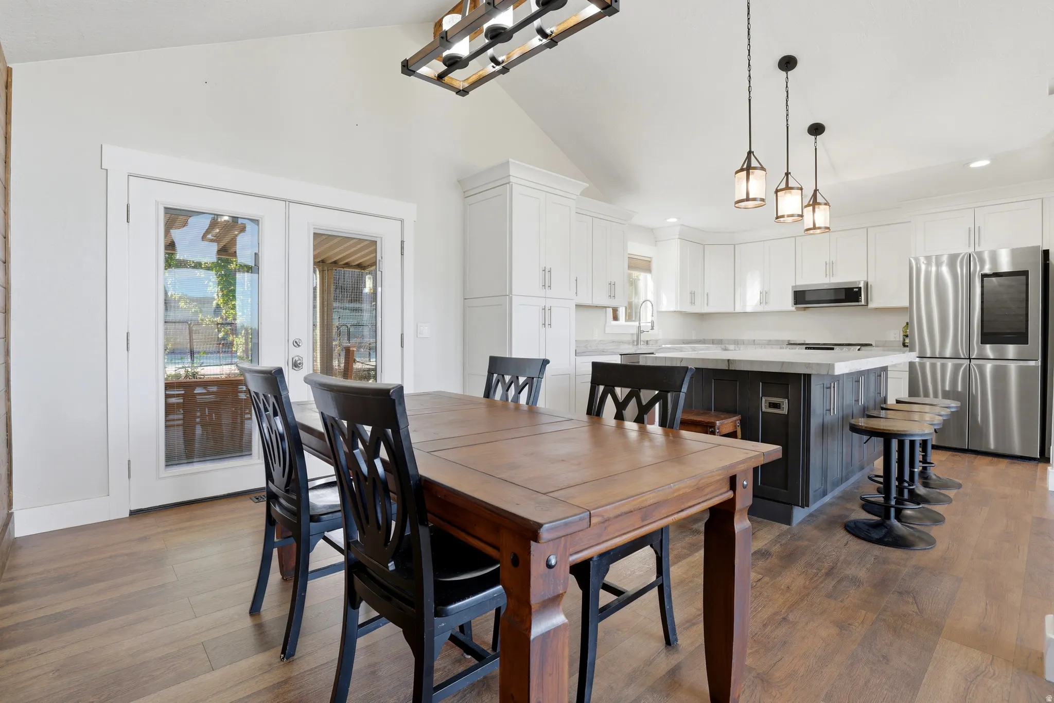 Vaulted ceiling, wood-finish flooring, white cabinetry, kitchen island with counter seating, stainless steel appliances