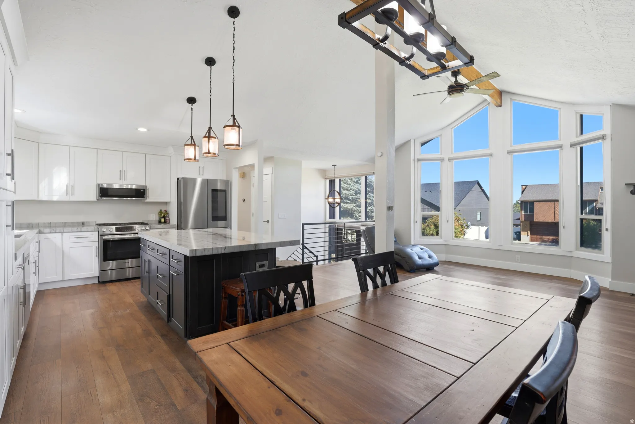 Expansive kitchen featuring stainless steel appliances, a large center island with pendant lighting, and wood-finish flooring