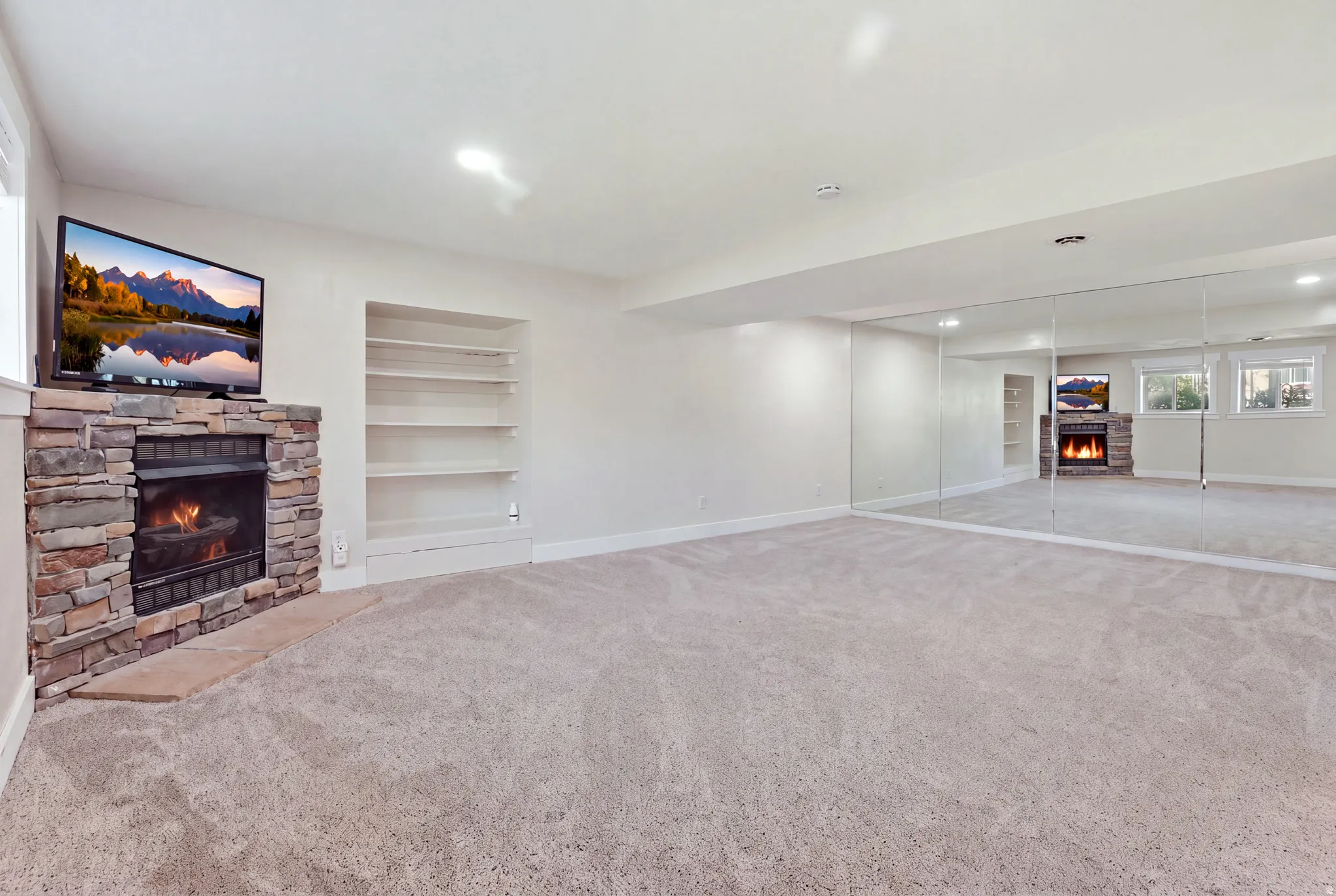 Recessed lighting, built-in shelving, stone-surround fireplace, wall-mounted mirrors, and carpet flooring