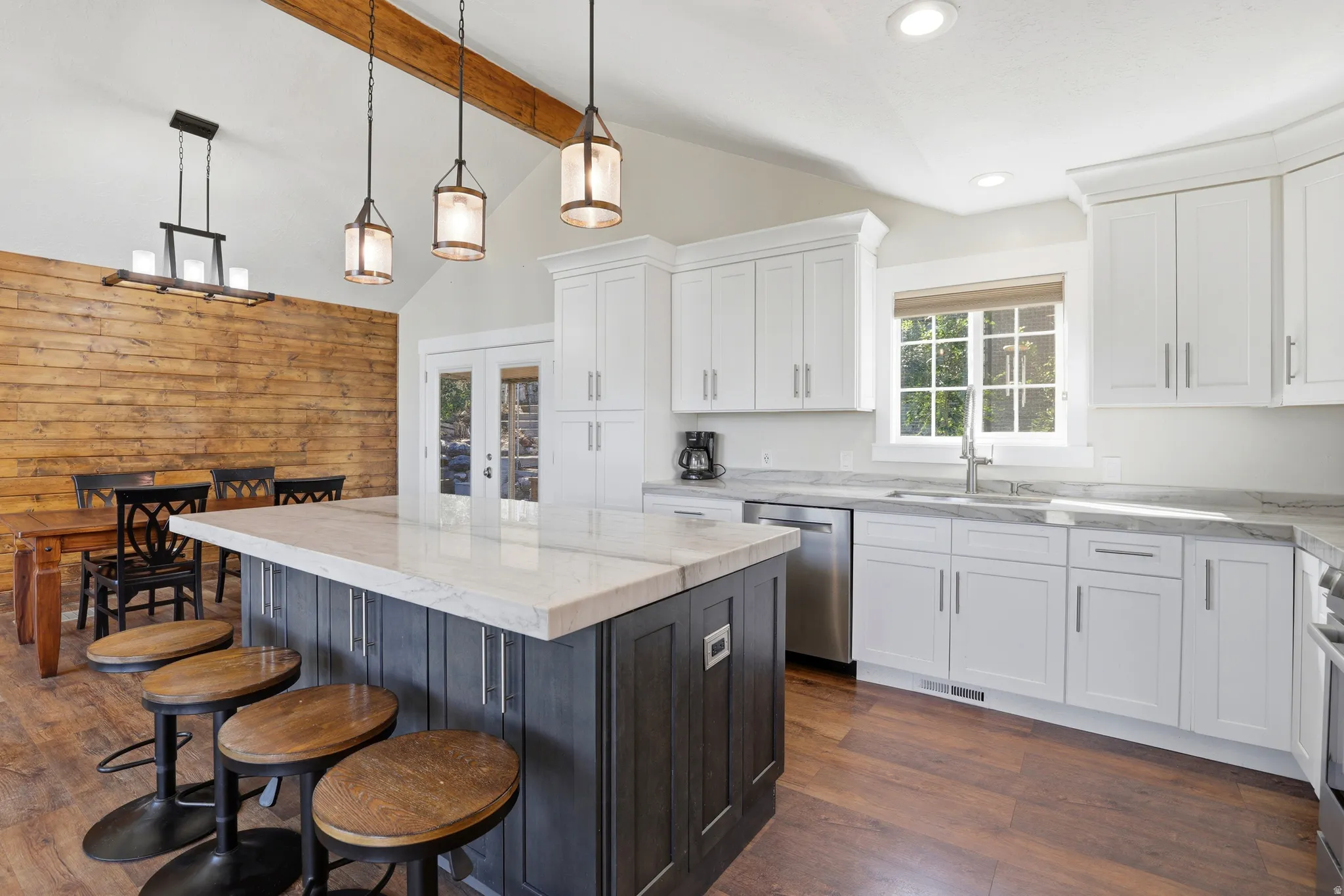 Vaulted ceilings with exposed wood beams, wood-finish flooring, white shaker cabinetry, stainless steel appliances, and a central island with countertop seating