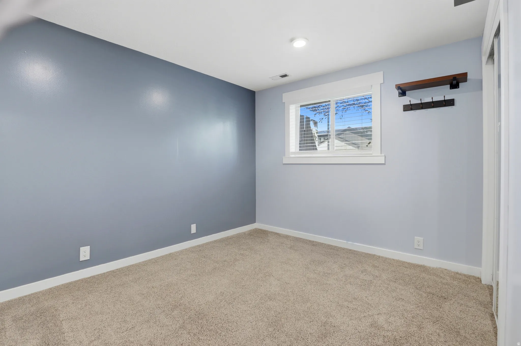 Neutral-toned carpeting, light blue wall paint, white trim, and a window with blinds
