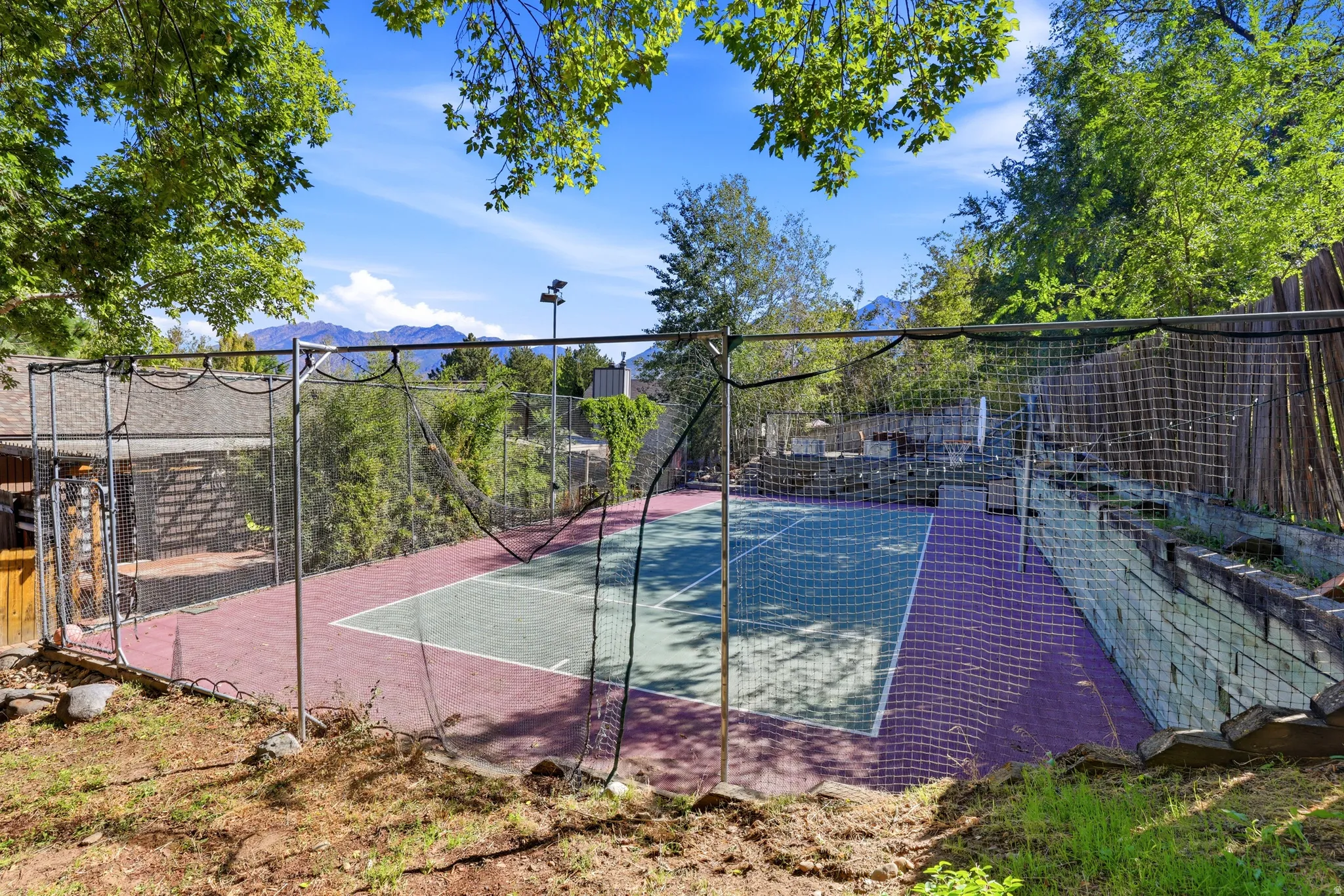 Outdoor sport court with perimeter netting, adjacent to a slatted wood fence and retaining wall