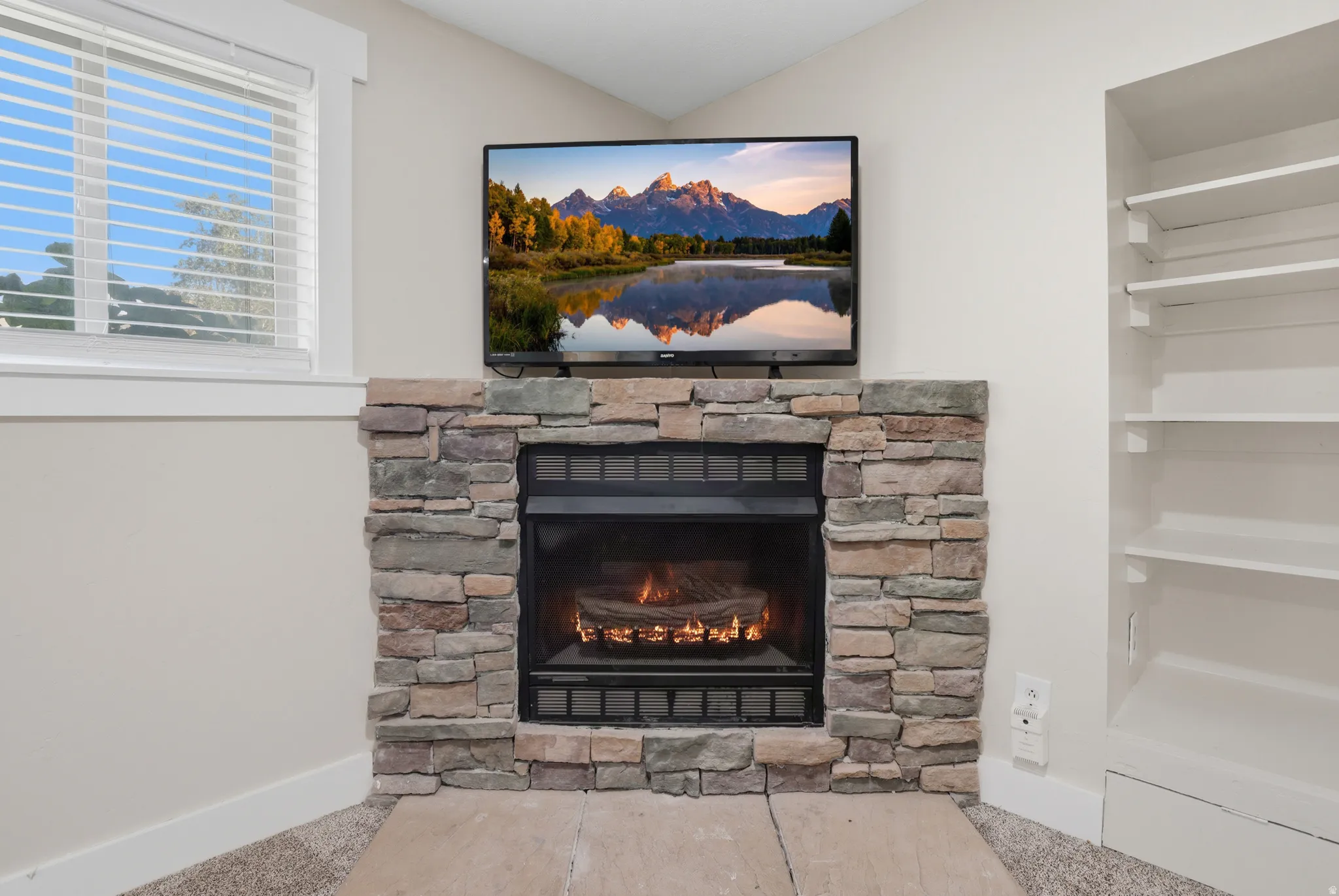 Stone-clad fireplace with hearth, built-in shelving, and window with blinds