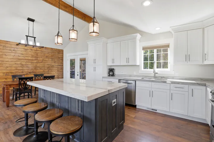 Vaulted ceilings with exposed wood beams, wood-finish flooring, white shaker cabinetry, stainless steel appliances, and a central island with countertop seating