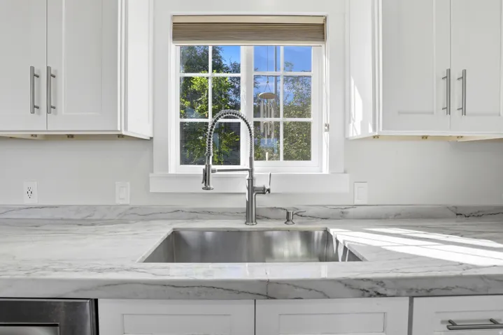 White shaker cabinetry with brushed nickel hardware, undermount stainless steel sink, gooseneck faucet, and stone countertops