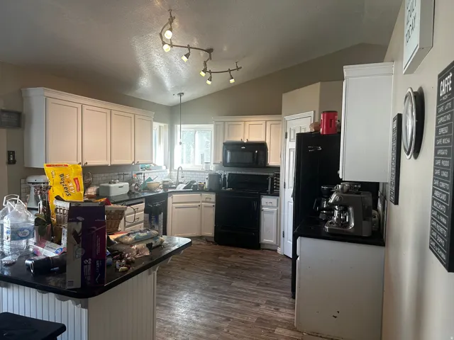 Kitchen featuring white shaker-style cabinetry, black countertops, and wood-finish flooring