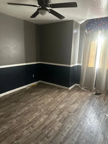 Wood-finish flooring with a horizontal plank pattern, ceiling fan with integrated lighting, and two-tone wall paint