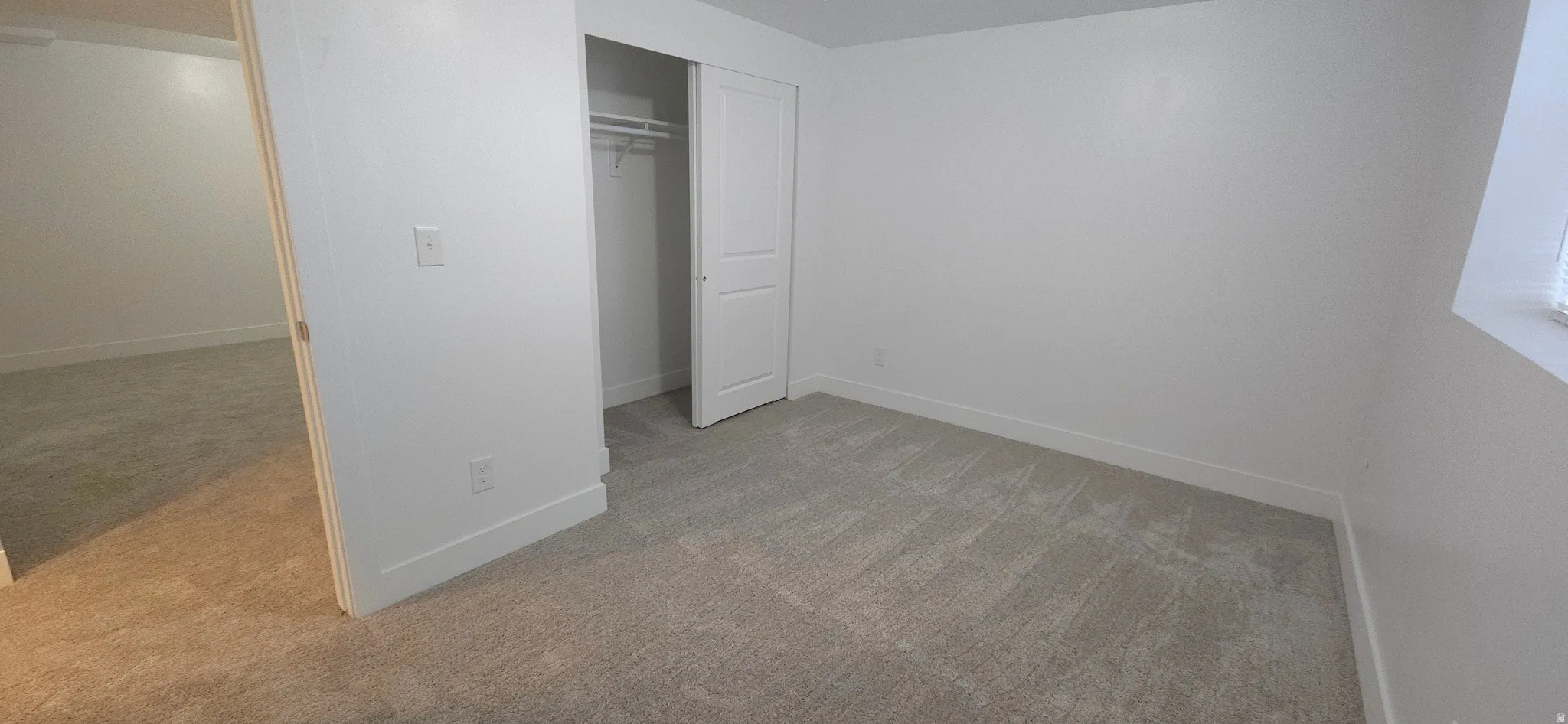 Neutral-toned carpeting, white walls, and a closet with a bi-fold door