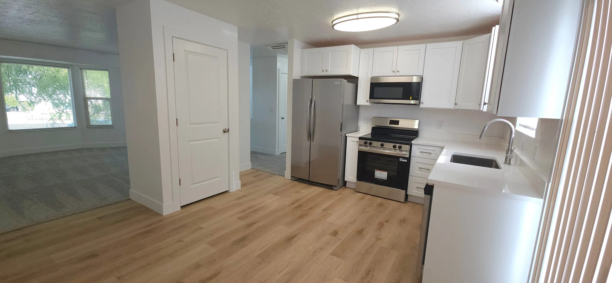 Modern kitchen with white cabinetry, stainless steel appliances, light-colored countertops, and wood-finish flooring