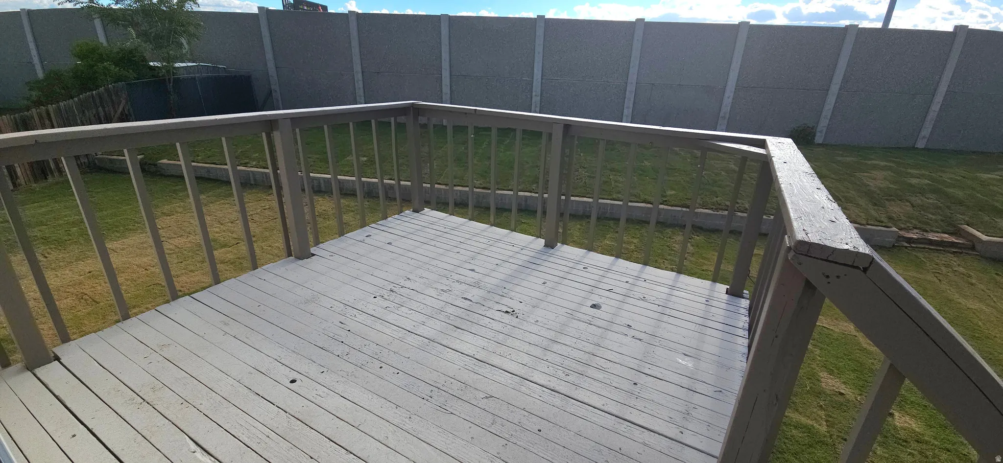 Outdoor wooden deck with railings, overlooking a grass area with a concrete perimeter wall