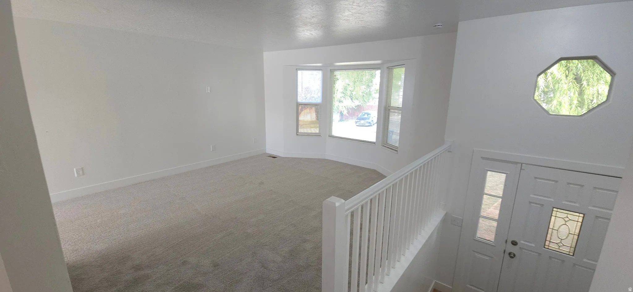 Expansive carpeted living area with a bay window, white walls, and a prominent octagon window above the entry