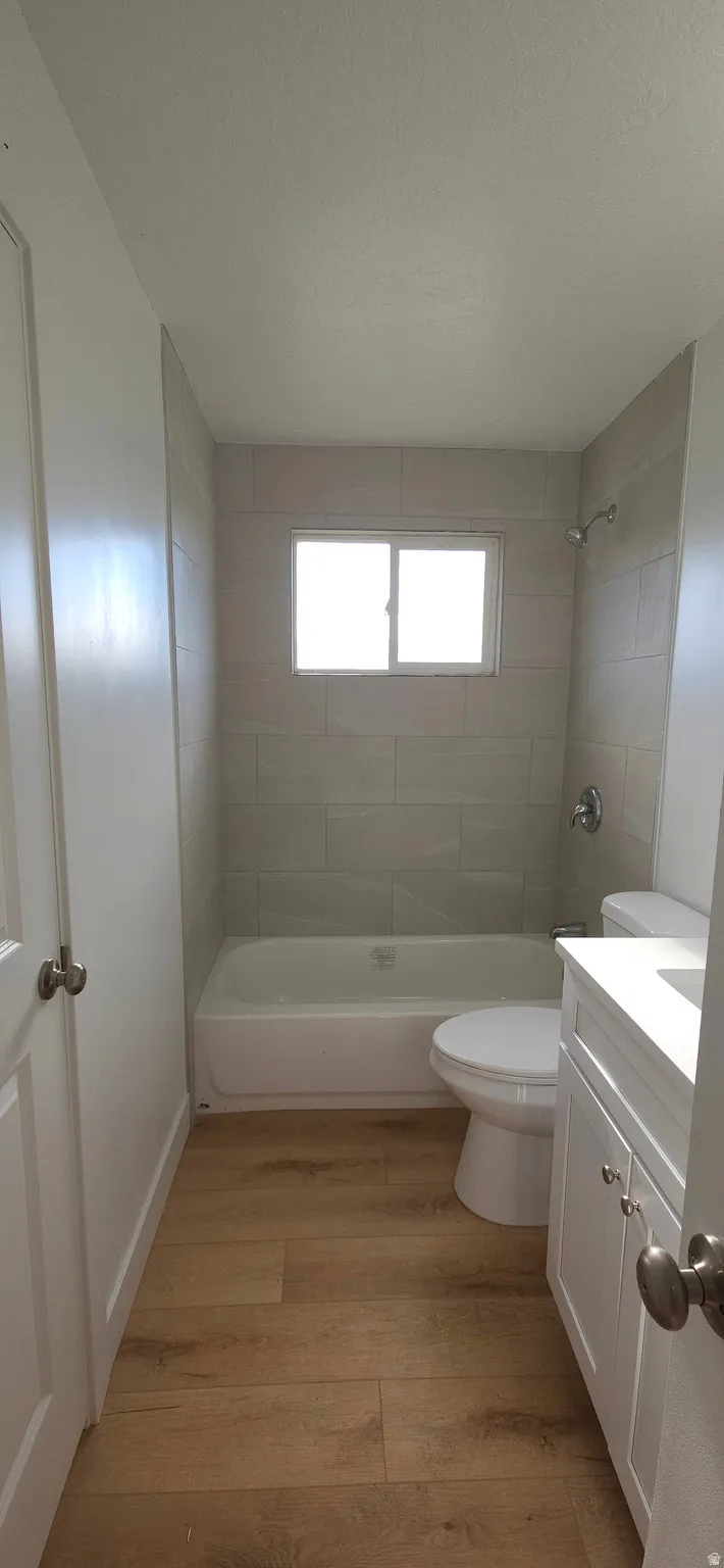 Bathroom featuring wood-finish flooring, a white vanity with cabinetry, a white bathtub, and a tiled shower surround