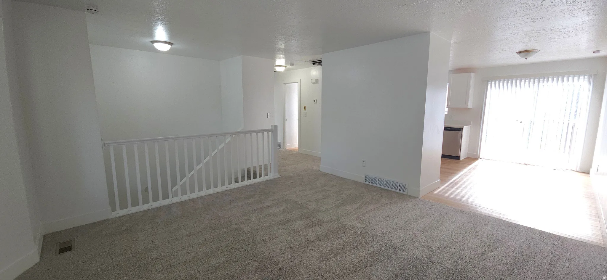 Carpeted living area with white baluster railing and neutral wall finishes