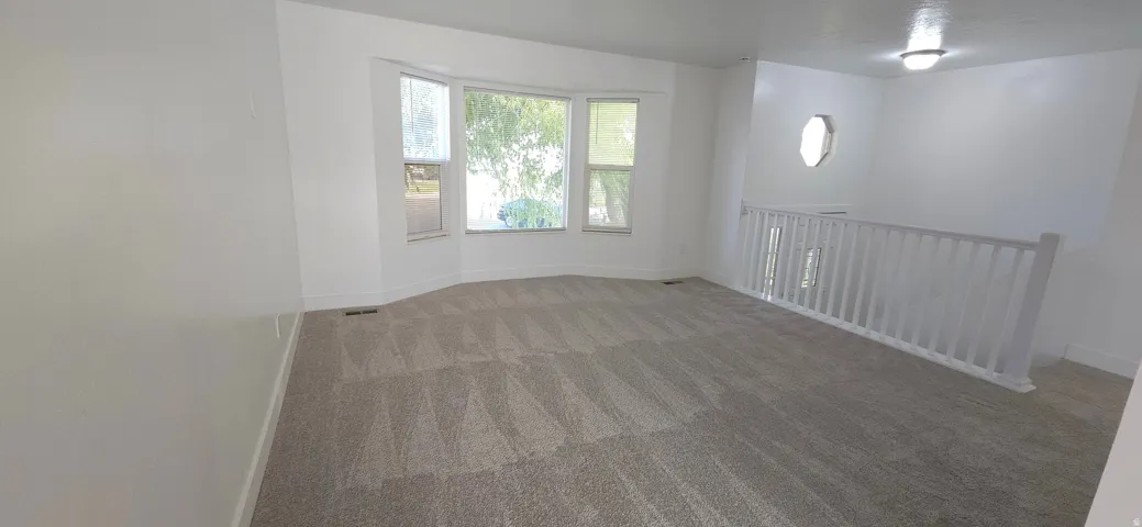 Spacious room featuring a bay window, neutral carpeting, white balustrade, and an upper window