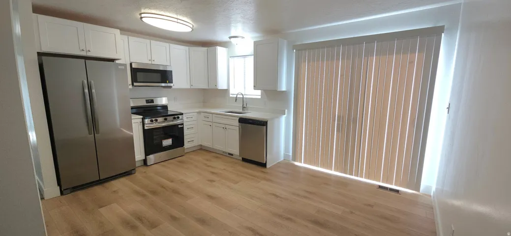 Modern kitchen featuring stainless steel appliances, white cabinetry with ample storage, wood-finish flooring throughout, and sliding glass doors opening to natural light