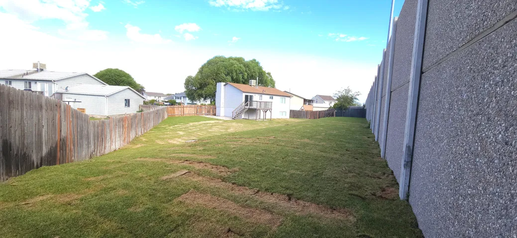 Expansive grassy yard with a wooden fence and a pre-cast concrete block fence