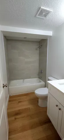 Bathroom featuring a white bathtub with subway tile surround, wood-finish flooring, white vanity with integrated sink, and chrome fixtures