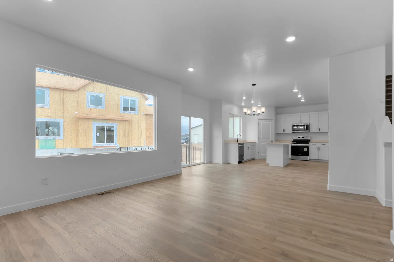 Open-concept living space with wood-finish flooring, recessed lighting, a large picture window, a sliding glass door, and a kitchen featuring white cabinetry, a center island, and stainless steel appliances