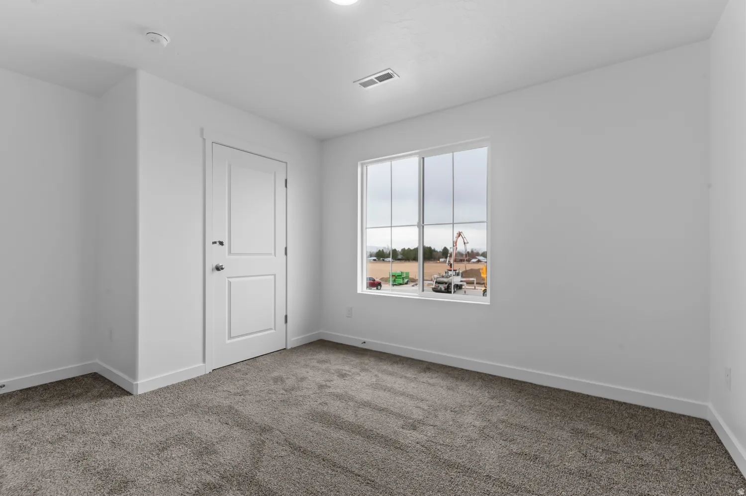 Neutral wall finishes, recessed ceiling lighting, textured carpeting, panel door with dark hardware, and a multi-pane window