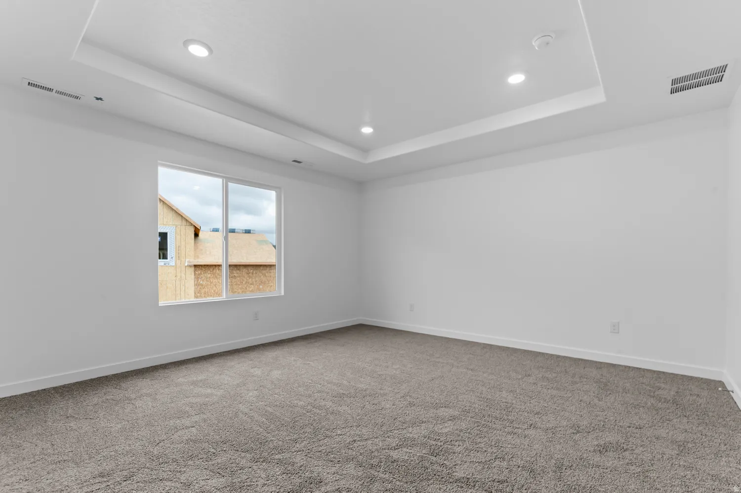 Recessed lighting, tray ceiling, neutral carpet, white walls, and a large window