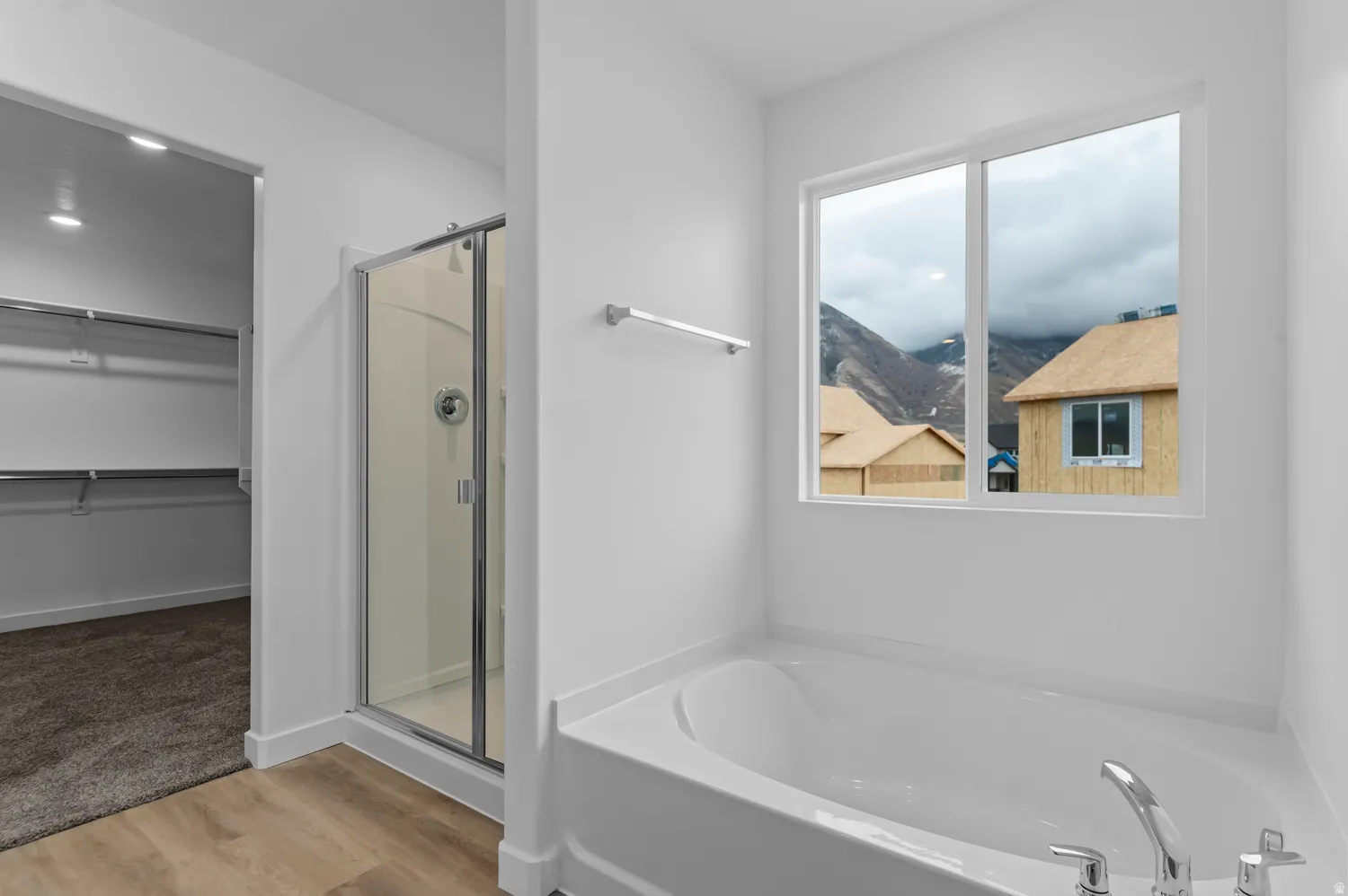 Deep soaking tub with chrome fixtures, clear glass shower enclosure, and a walk-in closet with built-in shelving
