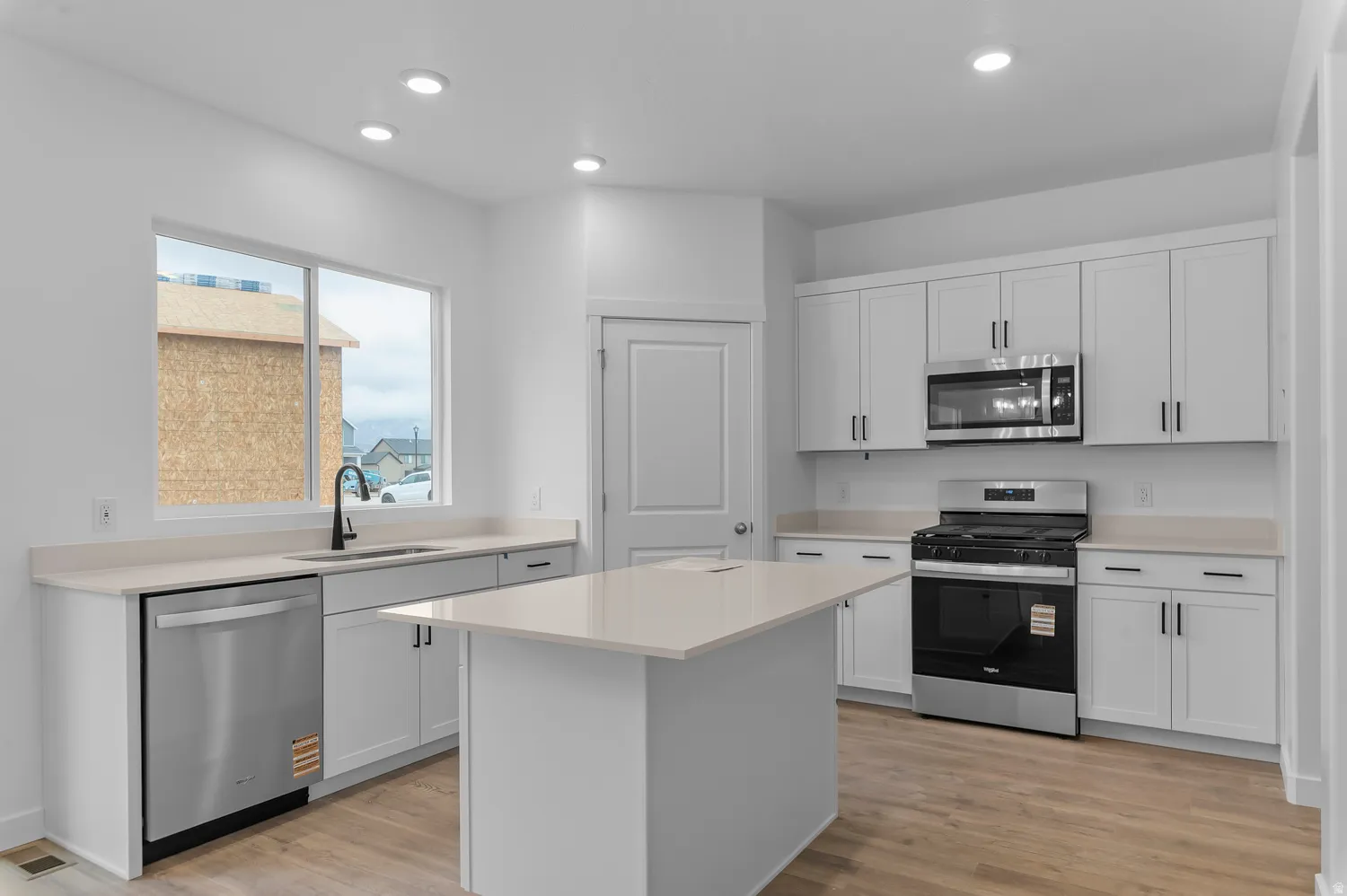 Modern kitchen featuring white cabinetry, light-toned countertops, stainless steel appliances, a central island, and wood-finish flooring