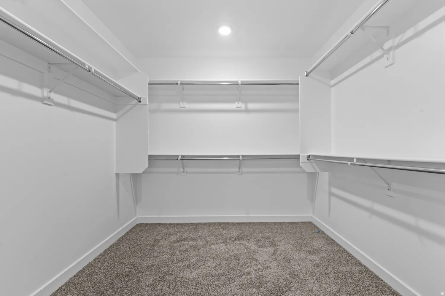 Walk-in closet featuring white built-in shelving, chrome hanging rods, and gray carpet flooring