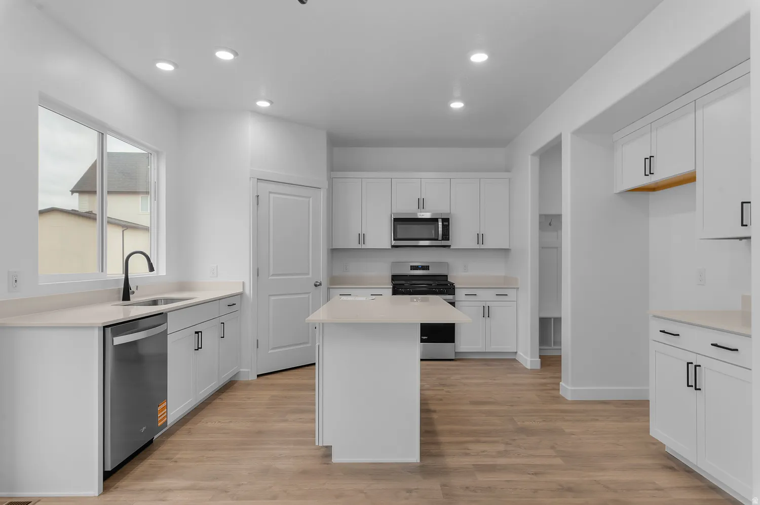 Modern kitchen featuring white cabinetry, light countertops, wood-finish flooring, recessed lighting, and stainless steel appliances