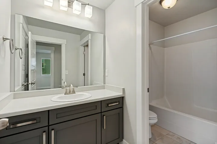 Vanity with a white countertop and dark cabinetry, an undermount sink with a brushed nickel faucet, an integrated shower-tub combination, and tiled flooring