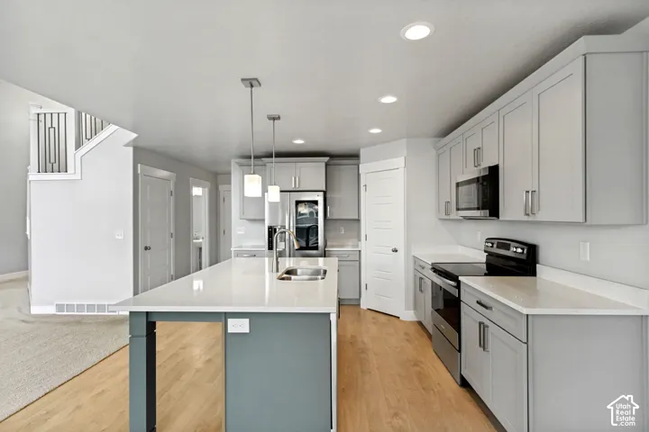 Kitchen featuring an island with pendant lighting, light-toned cabinetry, light countertops, wood-finish flooring, and stainless steel appliances